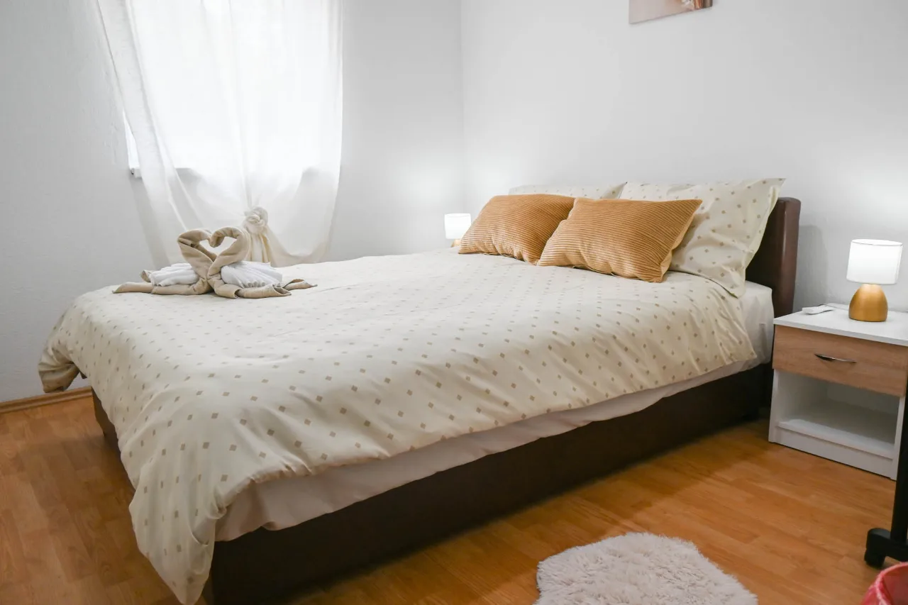 Spavaća soba apartmana sa bračnim krevetom, narandžastim jastucima, labudovima od peškira i noćnom lampom, laminat na podu